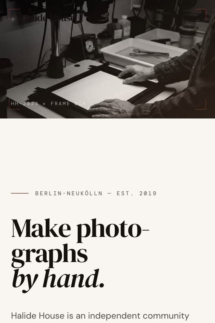 v0 mobile top crop with hands working beneath an enlarger in a black-and-white darkroom photograph above the serif hero